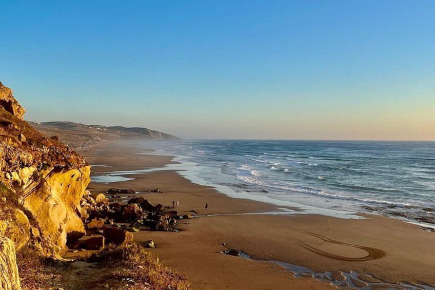 A coastal landscape with a sandy beach, rocky cliffs, and the ocean. 1