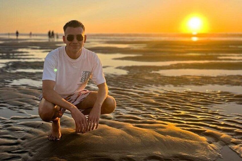 A person crouching on a sandy beach at sunset. 2