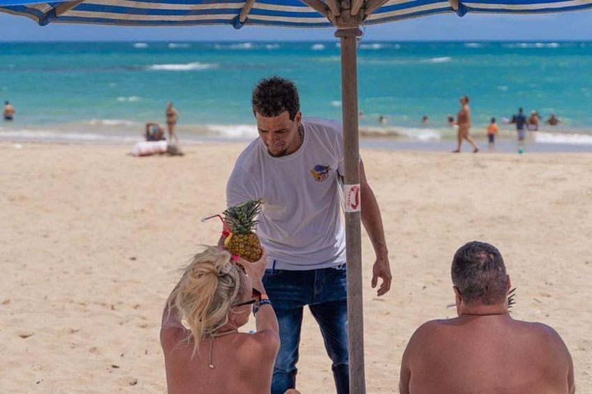 A beach scene with people, a man holding a pineapple, and a beach umbrella. 4