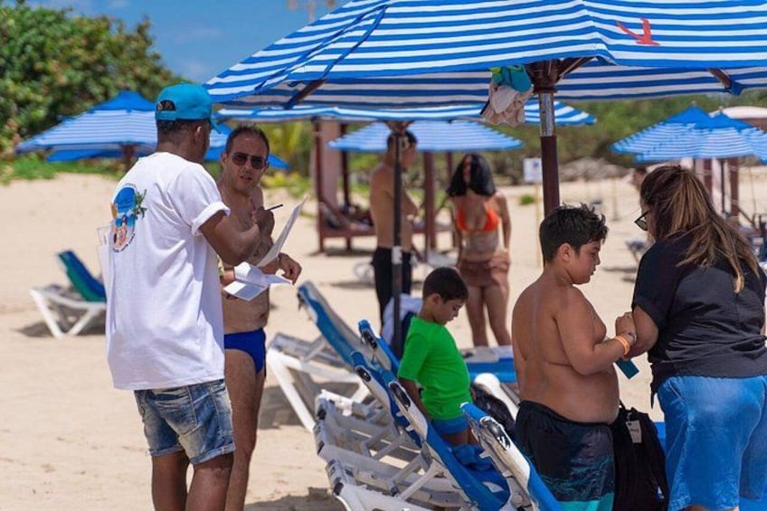 A beach with people under striped umbrellas, beach chairs, and a sandy shore. 2