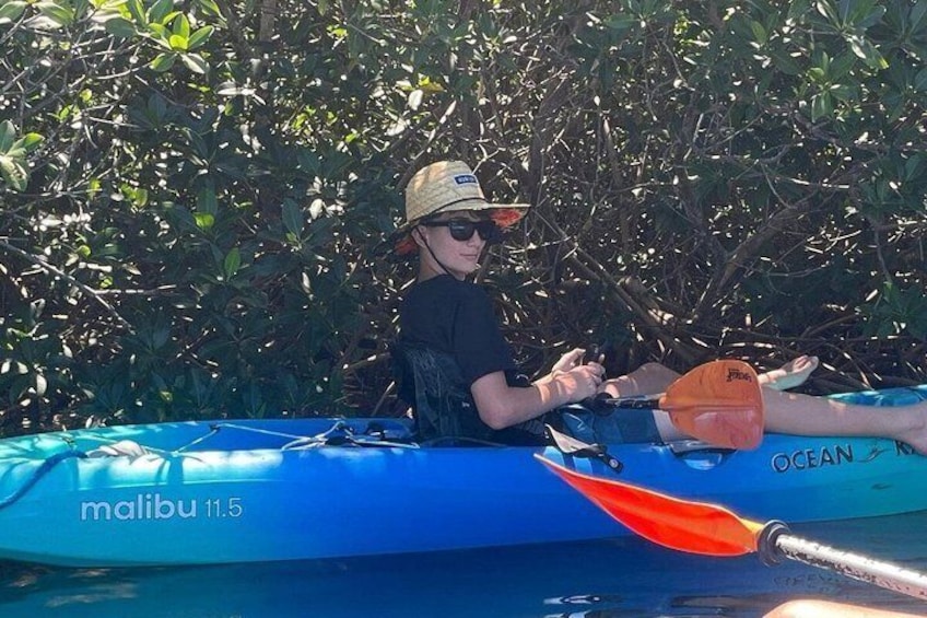 A person in a kayak with 'malibu 11.5' written on it, surrounded by dense foliage. 2