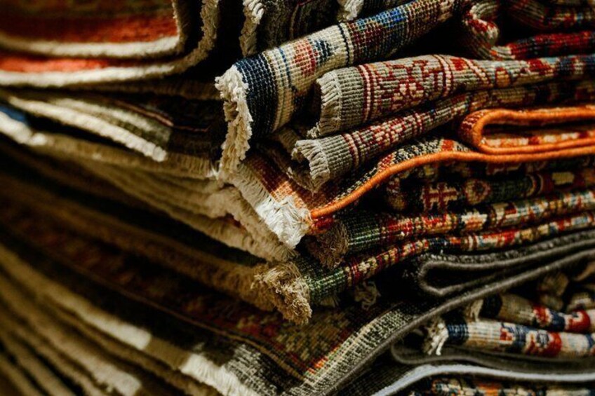 A variety of colorful woven rugs stacked together. 5