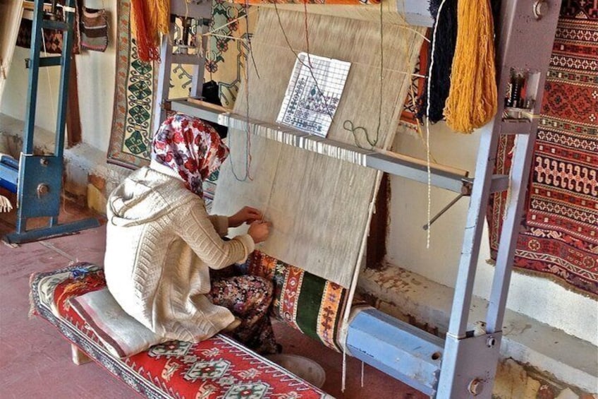 A person weaving on a loom with patterned textiles and tools around. 2