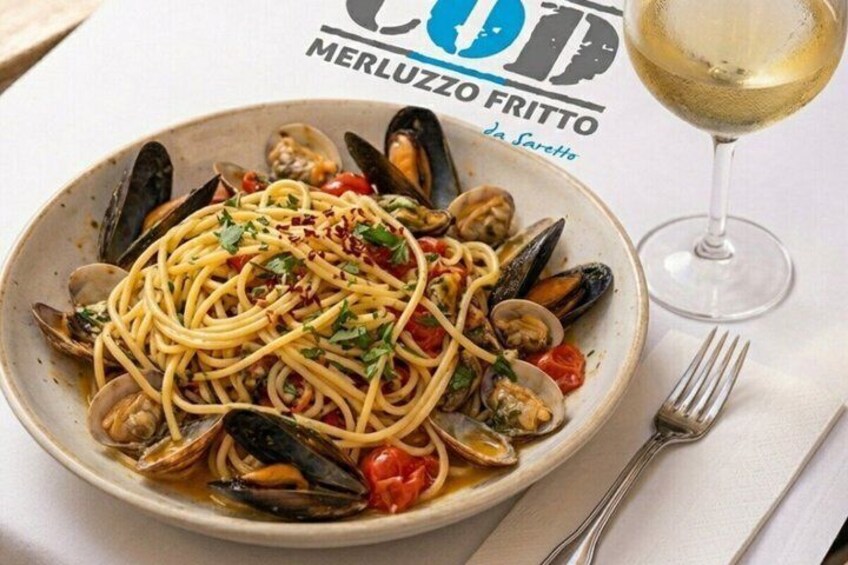 A plate of spaghetti with mussels, garnished with herbs, and a glass of white wine on the table. 2