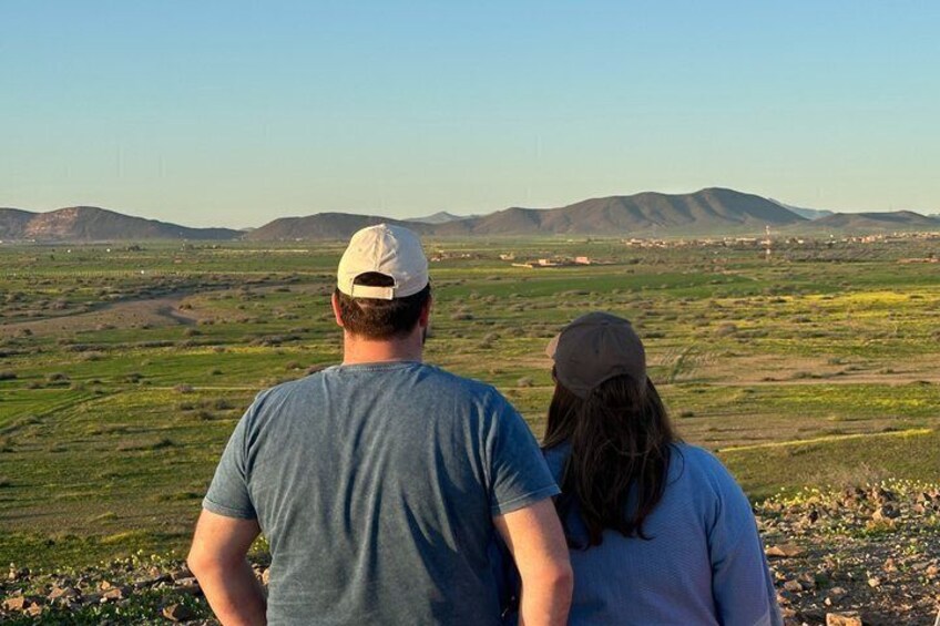Two people standing on a grassy hill overlooking a valley with distant mountains. 3
