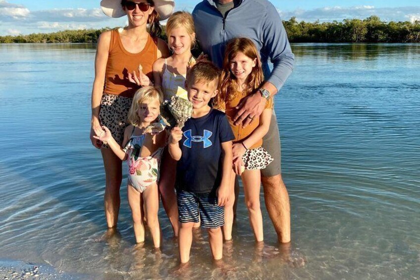 A family standing in shallow water with a clear view of the lake and distant trees. 3