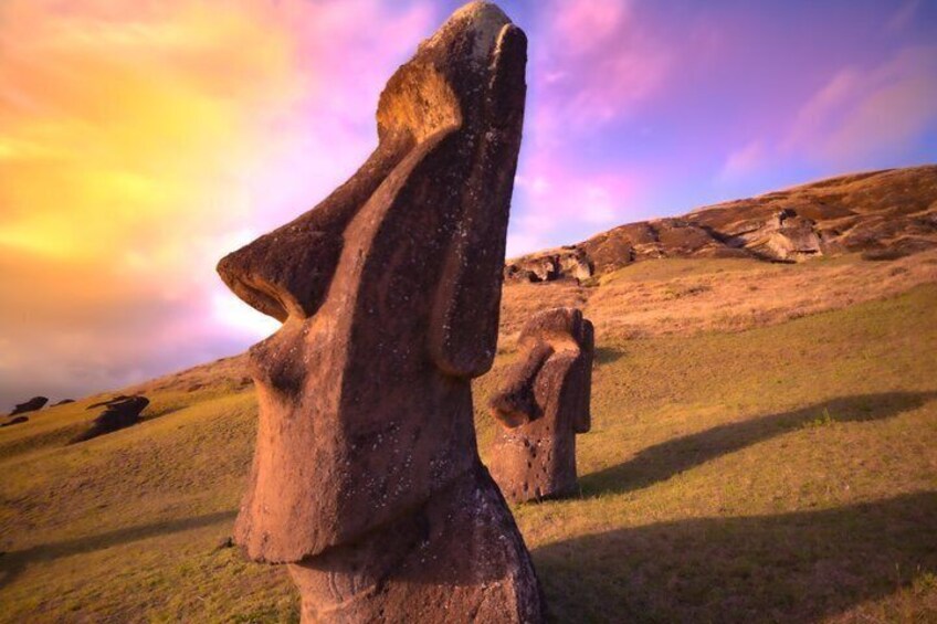 A large stone monolith with a carved figure, set against a grassy hillside under a colorful sky. 1