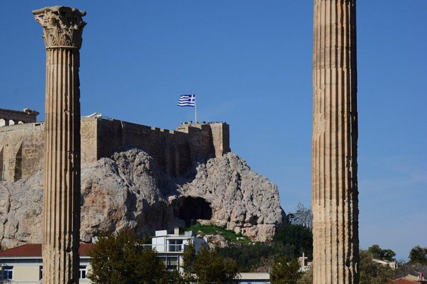 Ancient ruins with columns, a flag, and a rocky hill. 2