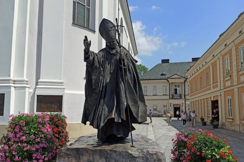 A statue of a historical figure in a courtyard with buildings and flowers. 3