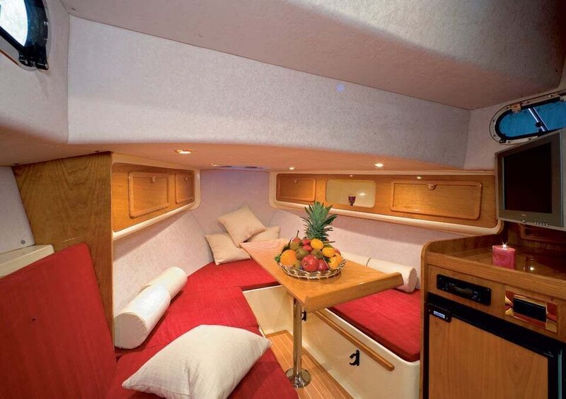 A compact interior with a red cushioned seating area, a wooden table with a fruit bowl, a television, and a small cabinet. 5