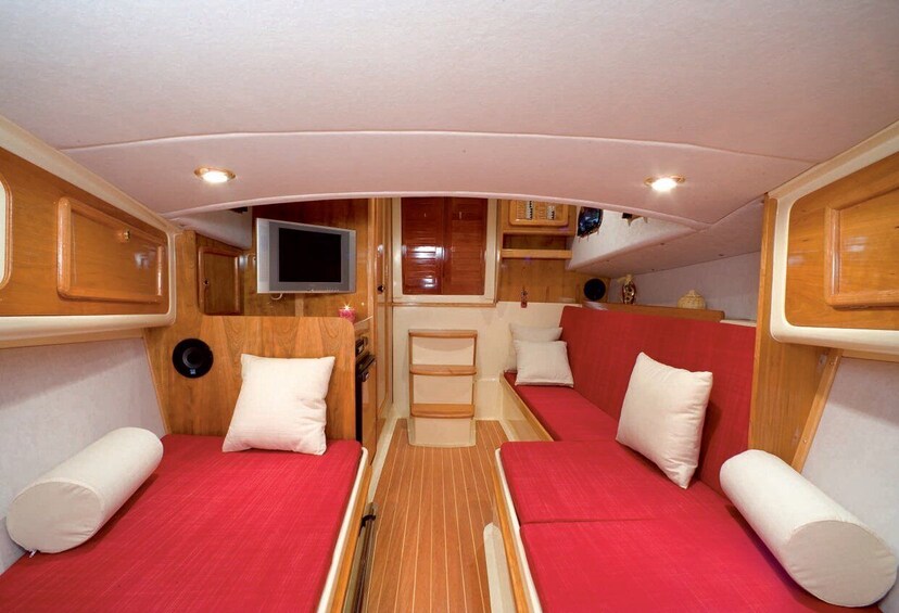 A compact interior with two red cushioned seating areas, wooden cabinetry, a television, and a small kitchen setup. 3