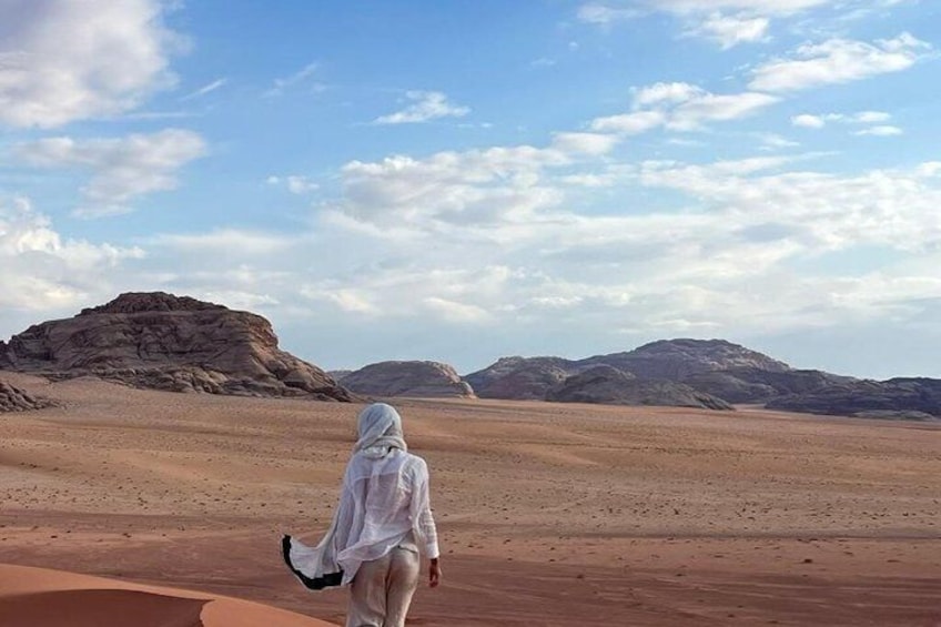 A person walking on a desert with sand dunes and mountains in the background. 1