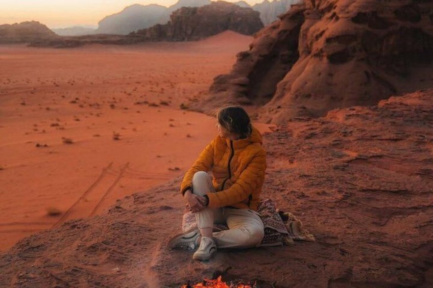 A person sitting on a rock by a campfire in a desert landscape. 5