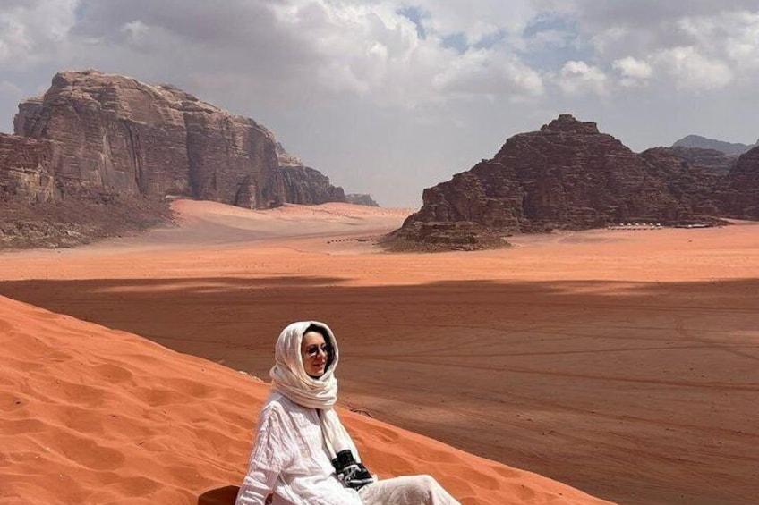 A person sitting on a sand dune with rocky formations in the background. 1