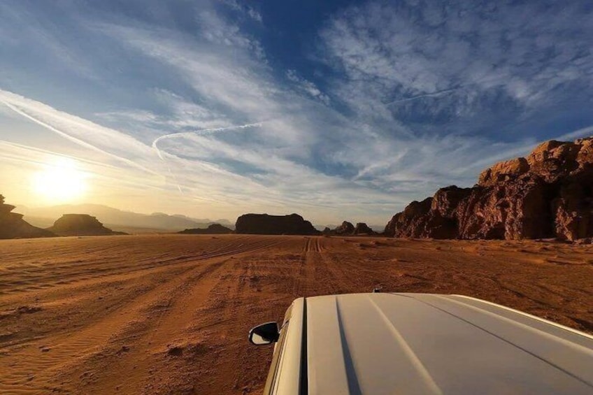 A desert landscape with a dirt road, rocky outcrops, and a vehicle. 2