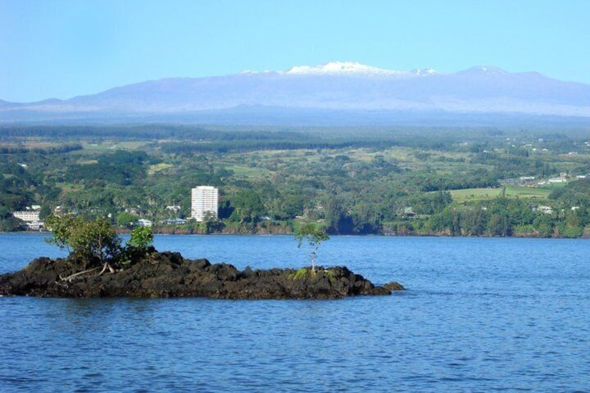 A volcanic island with a tree in the foreground, a lake, and a mountain range in the background. 2