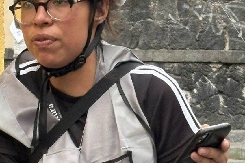 A person wearing a black and white jacket with a black strap across the chest, holding a smartphone. 5
