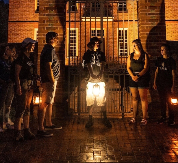 A group of people standing in front of a brick building at night with a metal gate. 3