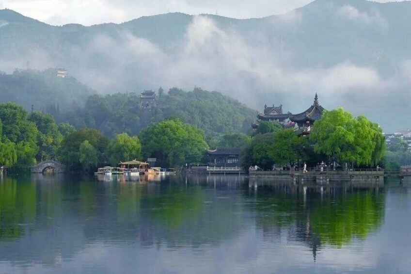 A serene lake with traditional architecture, including a pagoda and a pavilion, surrounded by lush greenery and misty mountains. 3