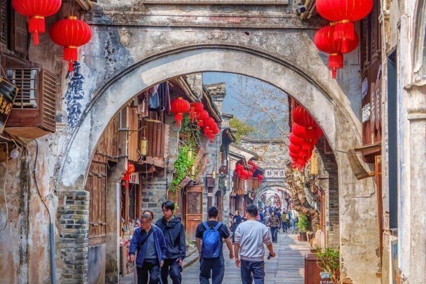 An archway with red lanterns, traditional wooden buildings, and people walking. 4