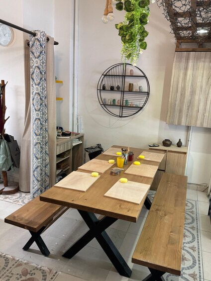 A wooden dining table with yellow placemats, a hanging plant, a wall-mounted shelf with decorative items, and a clock. 4