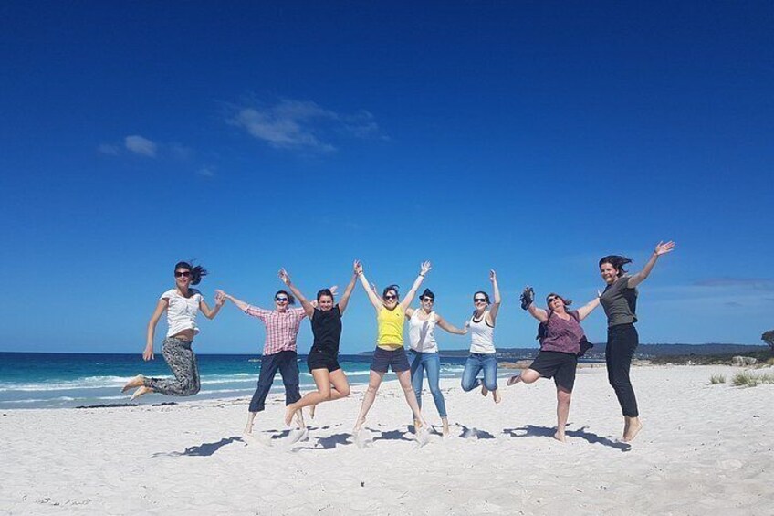 A group of people jumping on a beach with the ocean and clear sky in the background. 5