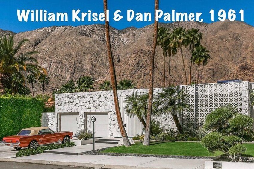 A red car parked in front of a white house with a stone facade, palm trees, and a mountain in the background. 2