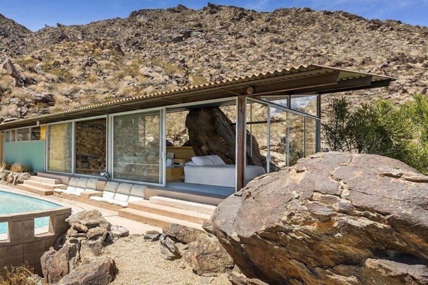 A modern house with a glass facade, a pool, and a large rock formation in the foreground. 4