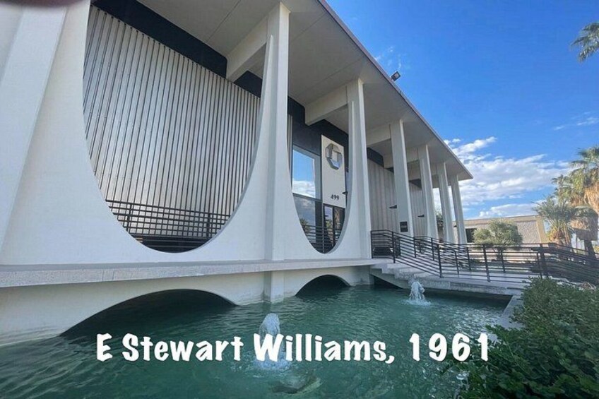 A modern architectural building with a unique circular window design, a bridge over water, and a clear sky. 3