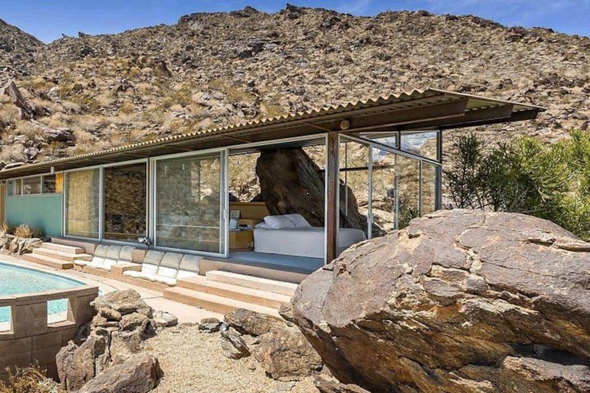 A modern house with a glass enclosure, a swimming pool, and a large rock formation in the foreground. 1