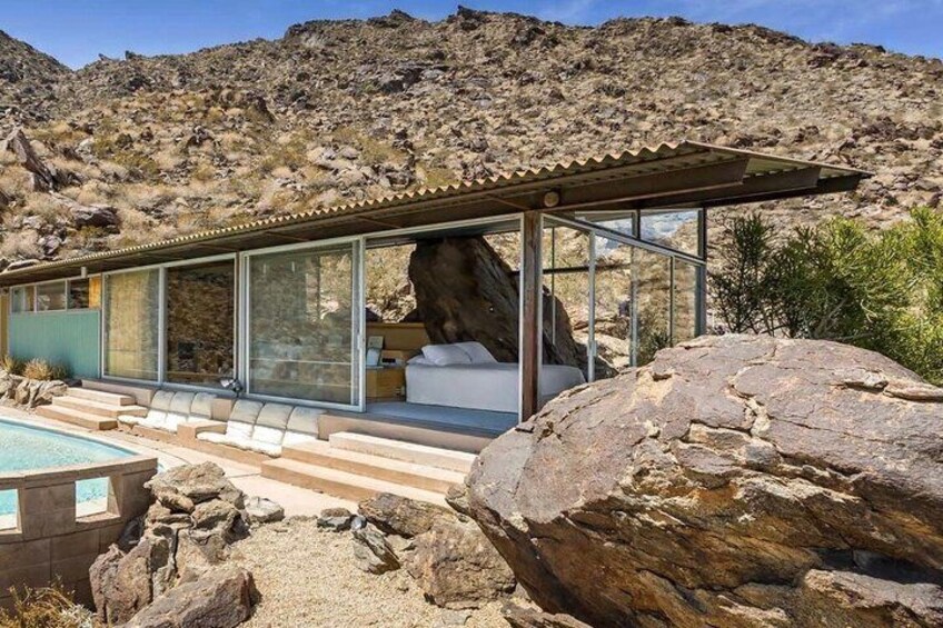 A modern house with a glass facade, a pool, and a large rock in the foreground. 1