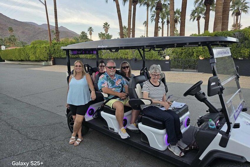 A golf cart with four people, palm trees, and mountains in the background. 5