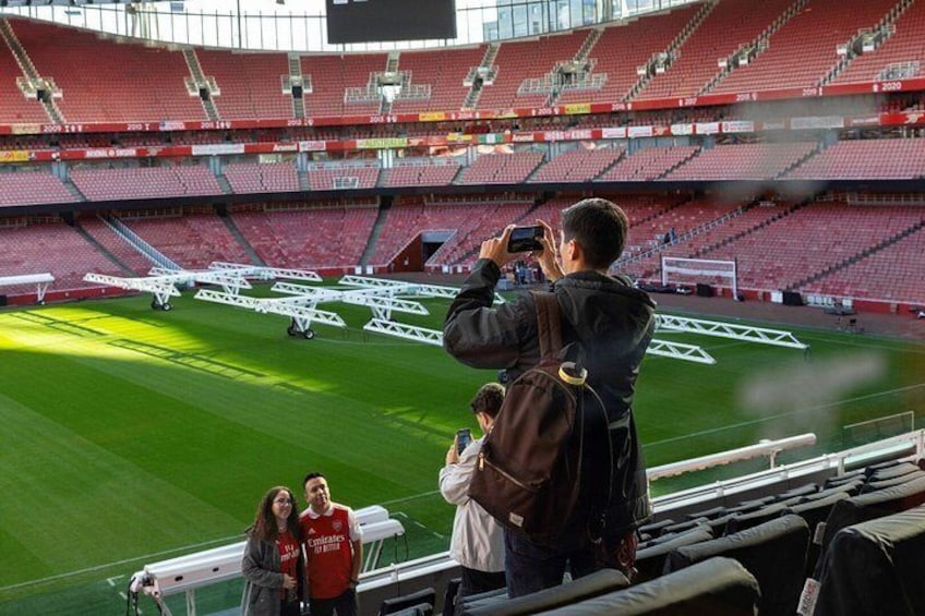 A stadium with empty red seats, a person taking a photo, and a few people standing on the sidelines. 2