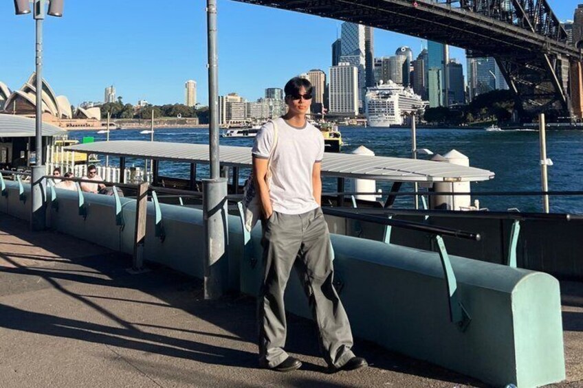 A person standing by a waterfront with a city skyline and a bridge in the background. 4