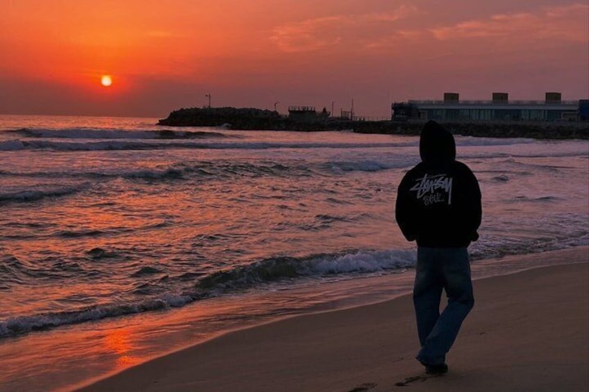A person standing on a beach facing the ocean at sunset. 1