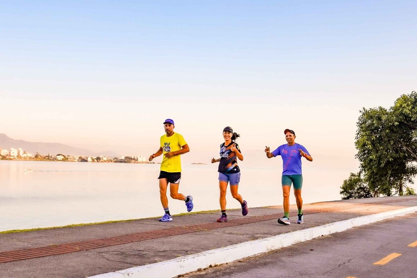 Three people running on a path by a calm body of water with a clear sky. 5