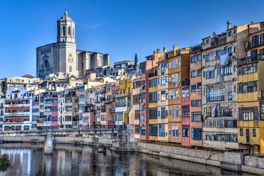 A waterfront cityscape with colorful buildings, a prominent church with a bell tower, and a calm river reflecting the architecture. 1