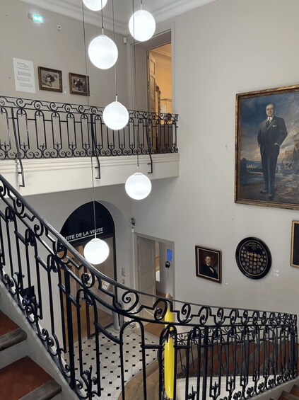 A staircase with ornate black railings, a painting of a man, and a plaque on the wall. 1