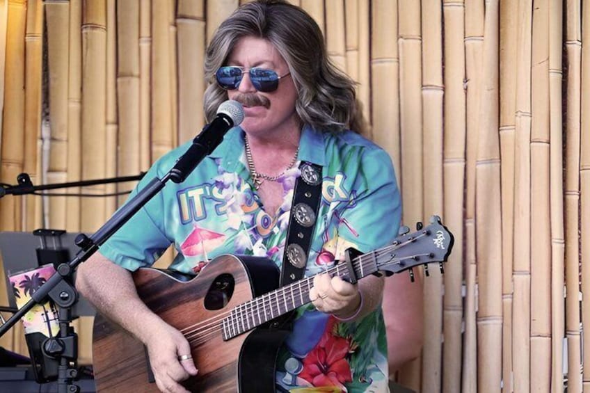 A person playing a guitar on stage with a microphone and a bamboo backdrop. 4