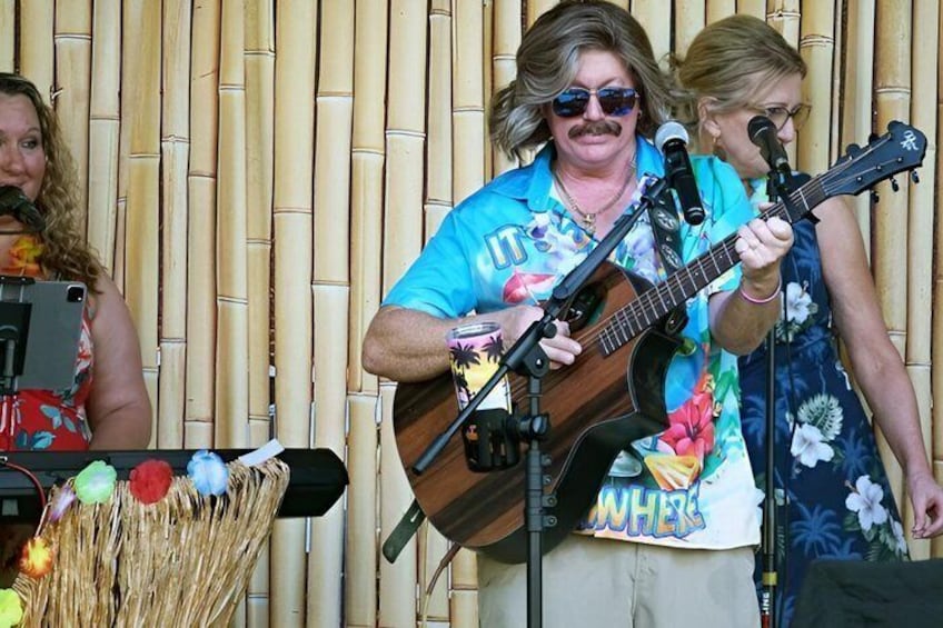 A person playing a guitar on stage with microphones and a bamboo backdrop. 5