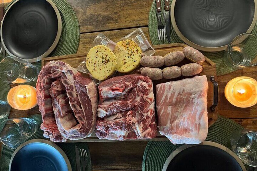 A wooden table with raw meat, sausages, and potatoes, set for a meal. 1