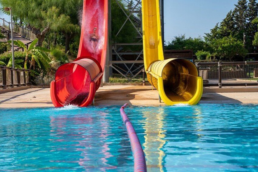 A water park with two slides, a pool, and surrounding greenery. 4