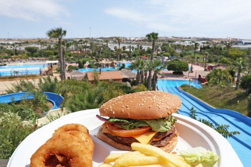 A plate with a burger, fries, and a fried item, with a water park and pool in the background. 2