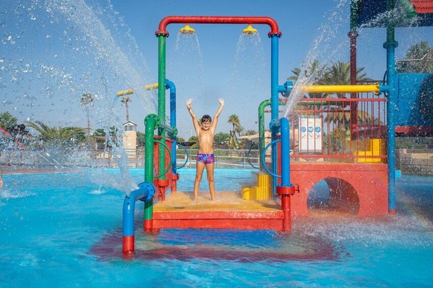 A water play area with a child standing on a platform, surrounded by colorful play structures and water jets. 3