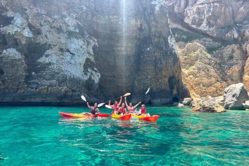 Three people kayaking in clear turquoise water with rocky cliffs in the background. 1