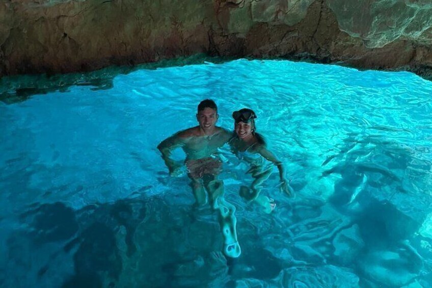 Two people swimming in a clear blue pool with rocky walls. 5