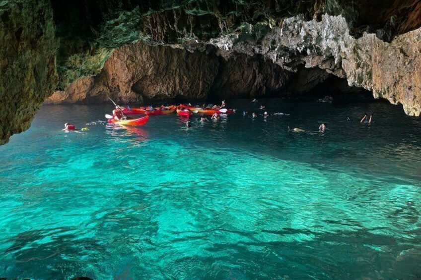 A group of kayaks and people in a clear blue water area under a rocky cave. 3
