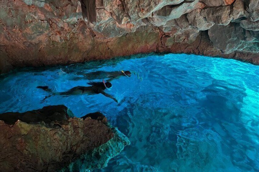 A swimmer in a clear blue pool with rocky walls. 2