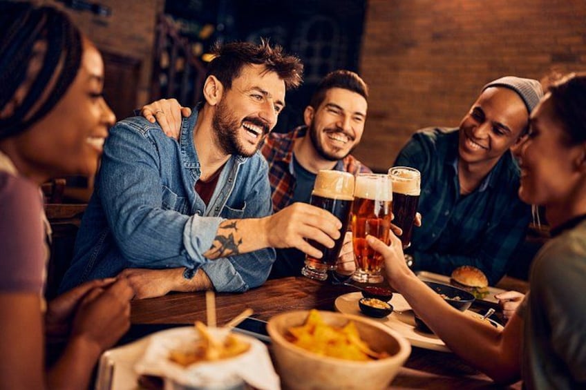 A group of people toasting with beer glasses at a table with food. 5