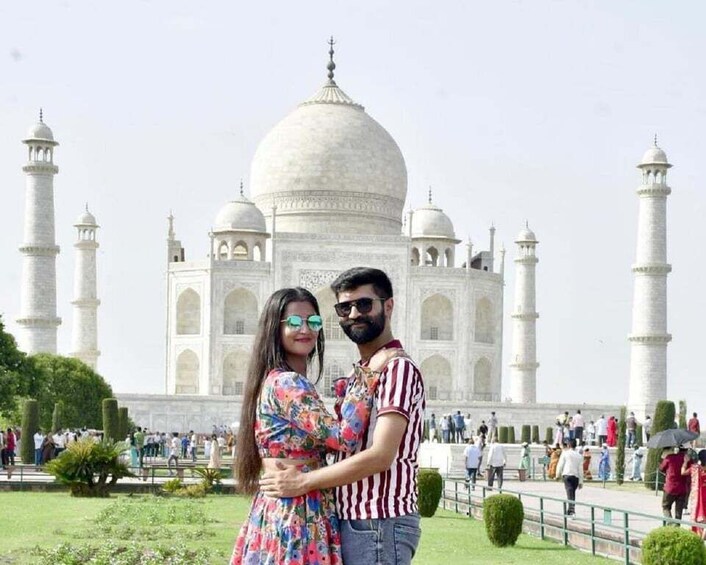 A couple standing in front of the Taj Mahal with the mausoleum and minarets in the background. 1